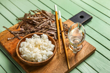 Cutting board with plate of boiled rice, vinegar, cut nori sheets and chopsticks on color wooden background, closeup
