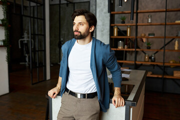 Successful calm peaceful businessman posing at loft apartment in stylish clothes leaning with hands...