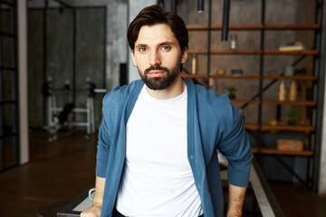 Indoor image of handsome man in white mockup shirt and blue cardigan in loft home interior, leaning...