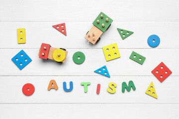 Word AUTISM with baby toys on white wooden background