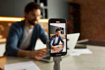 Selective focus of smartphone on tripod recording live video of successful businessman vlogger...