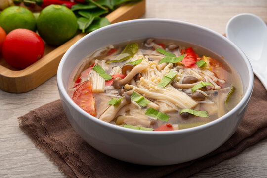 Thai vegan food ,Mushroom Tom Yum ,Spicy clear soup with enoki mushroom and brown shimeji mushroom in white bowl.