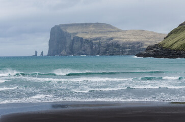Beach in Tjornuvik, small charming fishing village in Streymoy, Faroe Islands, Northern Europe, view to Risin og Kellingin, big waves on the sea during the rainy day