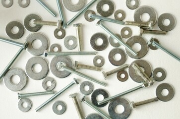 Close-up bolts, nuts and washers are scattered in a chaotic manner on a white background.  Flat lay...