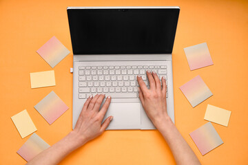 Female hands with modern laptop and sticky notes on orange background