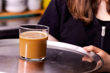 Waiter in black apron stretches a cup of coffee