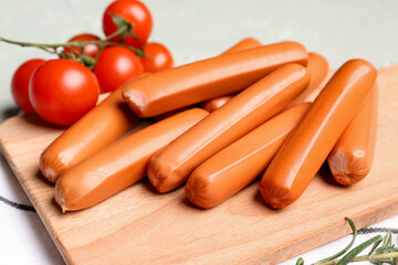 Wooden board with tasty sausages on light background, closeup