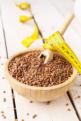 Bowl with buckwheat and yellow measuring tape on light wooden background. Diet concept