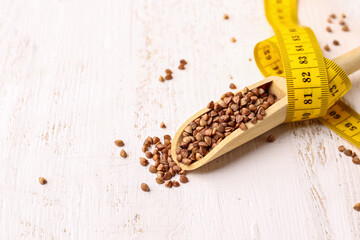 Spoon with buckwheat and yellow measuring tape on light wooden background. Diet concept