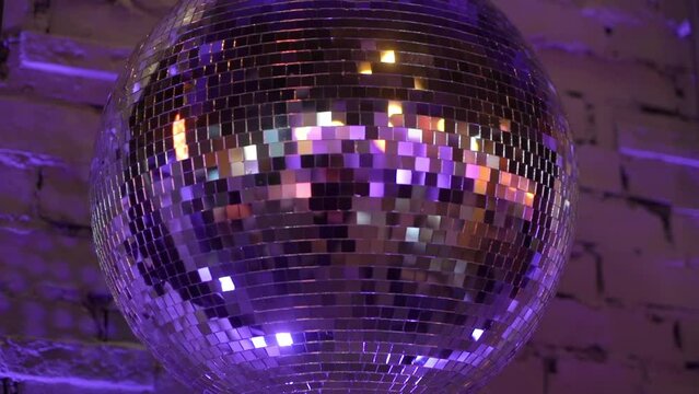 Silver mirror disco ball suspended from the ceiling rotates quickly, light spot rays and glare. White stage light at a concert hall, club, party or disco. Illumination and atmosphere.