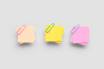 Beige, yellow and pink sticky notes with paper clips on grey background