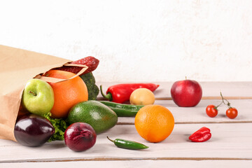 Paper bag with scattered vegetables and fruits on wooden table