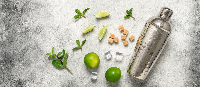 Mojito ingredients. Shaker, lime, mint leaves, cane sugar and ice cubes on a gray vintage background. Top view, flat lay, banner.