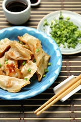 Plate with tasty Chinese jiaozi, onion and sauce on table