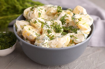 Bowl of tasty Potato Salad with greens on grey background, closeup