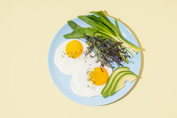Plate with tasty fried eggs and greens on beige background