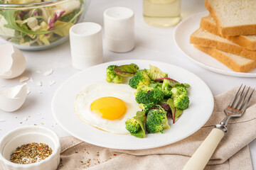Plate with tasty fried egg, broccoli and spinach on light background