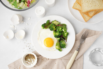Plate with tasty fried egg, broccoli and spinach on light background