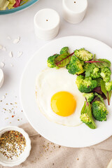 Plate with tasty fried egg, broccoli and spinach on light background