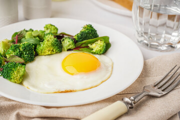 Plate with tasty fried egg, broccoli and spinach on light background