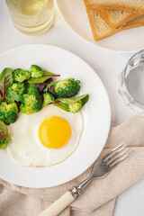 Plate with tasty fried egg, broccoli and spinach on light background