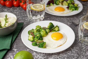 Plate with tasty fried egg, broccoli and spinach on grey grunge background