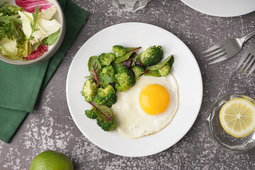 Plate with tasty fried egg, broccoli and spinach on grey grunge background