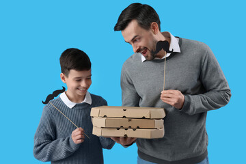 Portrait of father and his little son with paper mustache and pizza on light blue background