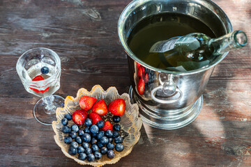Blueberries and strawberries in a serving plate on a wooden table. Top view. Glass of white wine with berries and an ice bucket for cooling alcoholic beverages - 590900714