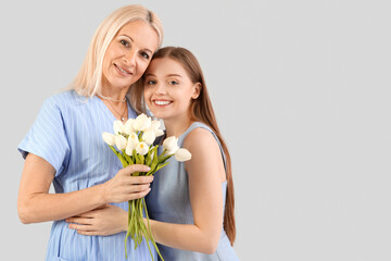 Fototapeta na wymiar Young woman greeting her mother with tulips on grey background
