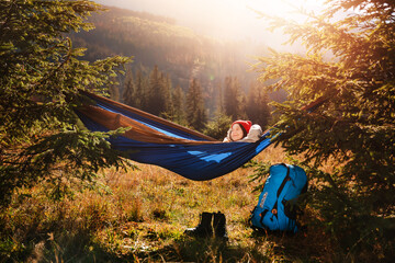 Teenage child lies asleep in tourist hammock on mountain landscape background. Sunny summer day. Recreation in the fresh air concept.