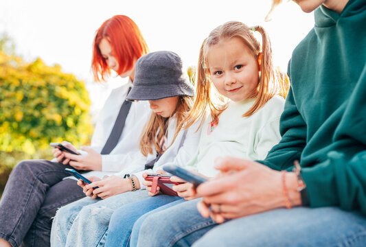 Little pretty girl portrait with sisters girls kids sitting in a row and browsing their smartphone devices. Careless young teenhood time and a modern technology concept image.