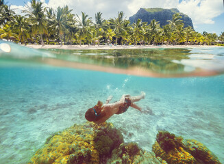 Diving teenage boy snorkeling over the coral reefs underwater photo in the clean turquoise lagoon on Le Morne palm trees beach with Le Morne Brabant mount. Mauritius island. Exotic traveling concept.