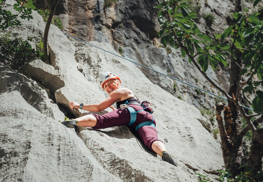 Smiling athletic woman in protective helmet climbing cliff rock wall using top rope and climbing harness in Paklenica National park site in Croatia. Active extreme sports time spending concept.