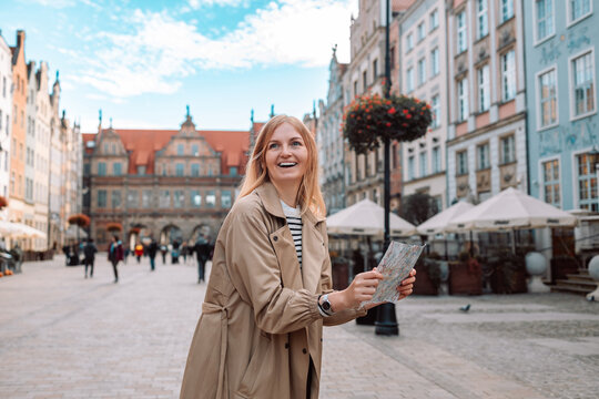 Attractive young female tourist holding a paper map on central square in Gdansk old town. Traveling Europe in autumn. High quality photo