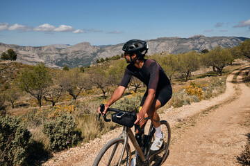 Man riding gravel bike on gravel road in mountains with scenic view.Professional cyclist practicing on gravel road.Male cyclist wearing black cycling kit and helmet.Cycle camp in Calpe, Alicante,Spain