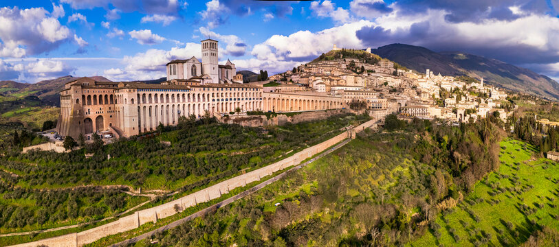 Assisi drone panoarama 8k of Sacro Convento monastery with dramatic light in Italy. Aerial view of medieval town and arches with cloudy sky. Umbria travel italian heritage site