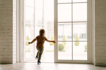 The boy runs out of the house, a big sunny window