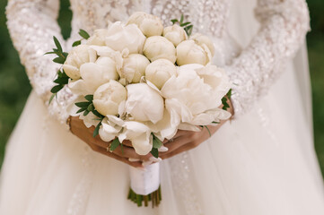 Beautiful white wedding bouquet of peonies in the hands of the bride