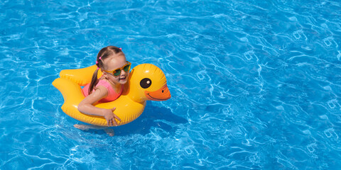 A banner with a cute child in sunglasses floating on an inflatable circle in the shape of a duck. A hot clear sunny summer day