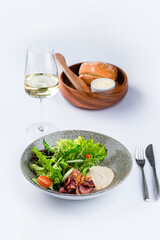 Green salad with beef meat, tomatoes, cucumbers, lettuce and sauce with a glass of wine.