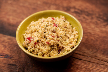 salad of couscous, spices and tomato tabbouleh in a yellow plate on a wooden background.