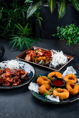 Asian food set of chicken fillet with shiitake mushrooms, onion, celery, sweet pepper and crispy squid rings in dough with sauce and microgreens on dark background.
