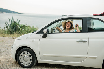 Car driver woman smiling showing new car keys and car copy space. Female driving rented cabrio on...