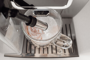 Coffee drink with milk foam in a coffee machine. Home coffee machine. Coffee with milk. Glass cup. Morning coffee. Coffee break. Barista job. Tasty warming drink.