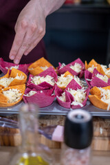 A man adds cheese from a white bowl to the colorful salty baskets. The salt and oil dishes on the table are blurred in the foreground.