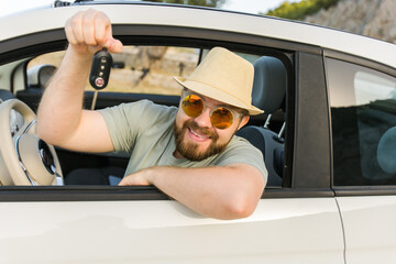 Car driver man smiling showing new car keys and car. Bearded guy driving rented cabrio on summer...