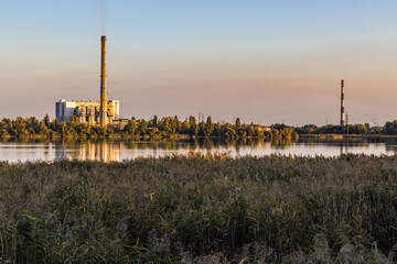 A waste processing plant at sunset on a lake, with chimneys belching smoke. Though energy's...