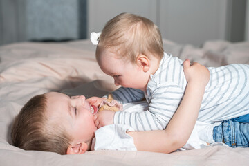 Older brother play with younger sibling lying in parent bed on bedroom. Happy Childhood carefree. Brother and sister spend time together, exploring and having fun