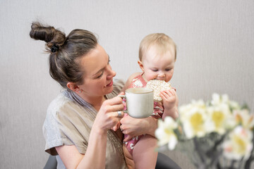 Family mother and cute baby eating breakfast at home child drinking from mother's cup. Infant tasting solid food, adult's meal. First steps Copy space